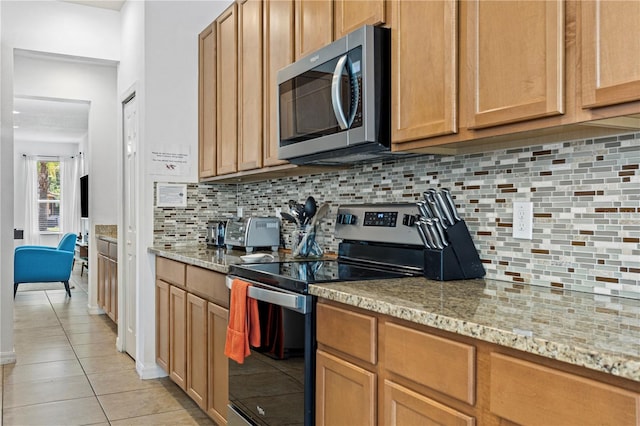 kitchen featuring light tile patterned floors, light stone counters, stainless steel appliances, and decorative backsplash