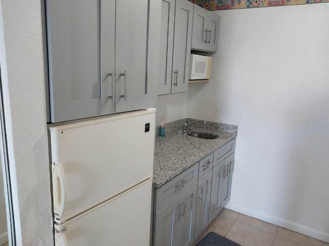 kitchen featuring light tile patterned flooring, white appliances, light stone countertops, gray cabinets, and sink