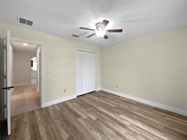 unfurnished bedroom featuring a textured ceiling, ceiling fan, a closet, and hardwood / wood-style flooring