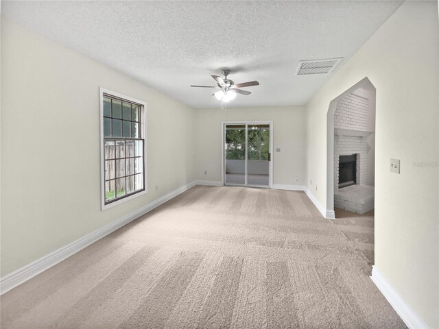 spare room with a textured ceiling, plenty of natural light, ceiling fan, and a fireplace