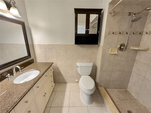 bathroom with a tile shower, tile walls, tile patterned flooring, vanity, and toilet