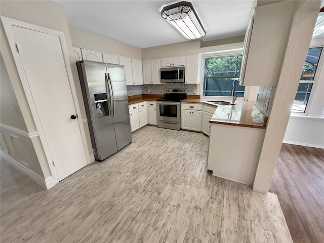 kitchen with white cabinets, backsplash, stainless steel appliances, light wood-type flooring, and sink