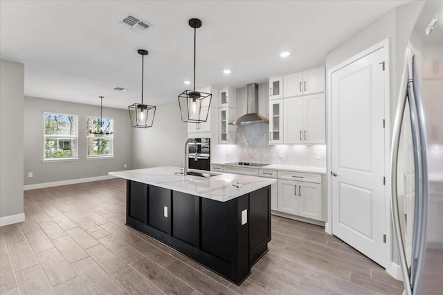 kitchen with sink, an island with sink, white cabinets, stainless steel refrigerator, and wall chimney exhaust hood