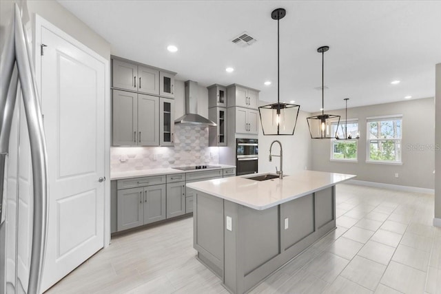 kitchen featuring pendant lighting, an island with sink, sink, wall chimney exhaust hood, and appliances with stainless steel finishes