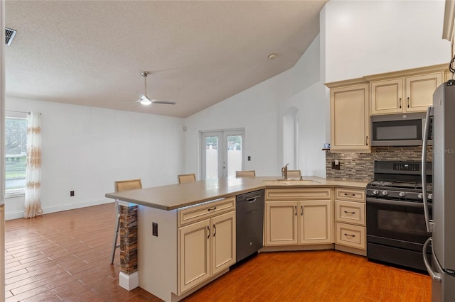 kitchen featuring kitchen peninsula, cream cabinetry, vaulted ceiling, and black appliances