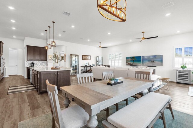 dining area with dark hardwood / wood-style flooring, ceiling fan with notable chandelier, wine cooler, and plenty of natural light