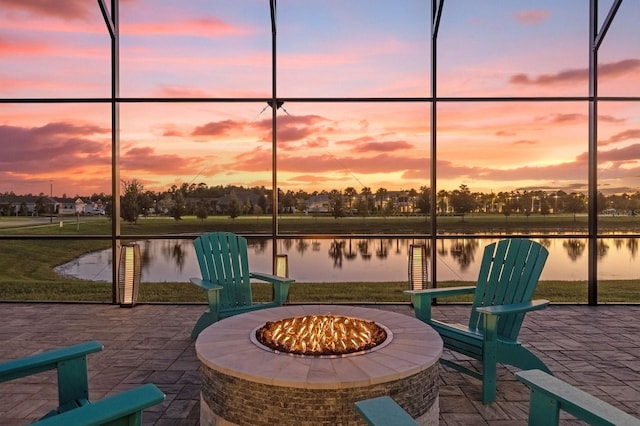 patio terrace at dusk with a fire pit, glass enclosure, and a water view