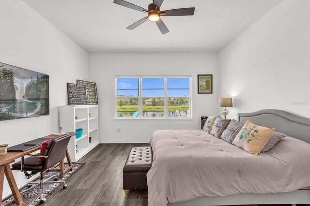 bedroom with dark hardwood / wood-style floors, ceiling fan, and a water view