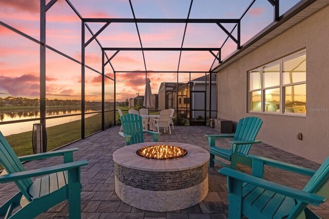 patio terrace at dusk featuring a lanai, a water view, and a fire pit