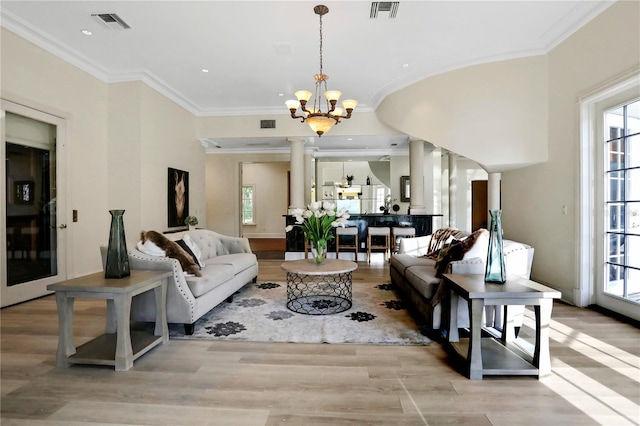 living room featuring an inviting chandelier, light hardwood / wood-style floors, crown molding, and ornate columns