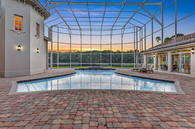 pool at dusk with glass enclosure and a patio area