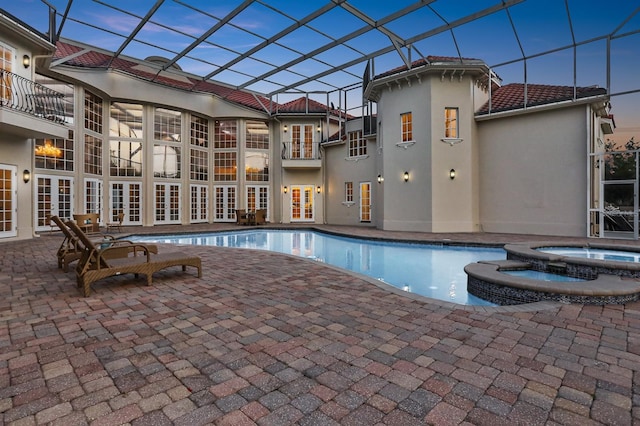 pool at dusk featuring a patio, an in ground hot tub, and glass enclosure