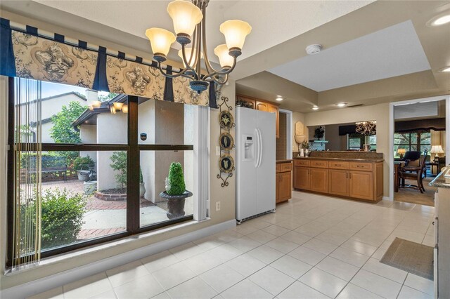 kitchen with a tray ceiling, white refrigerator with ice dispenser, an inviting chandelier, light tile patterned floors, and decorative light fixtures