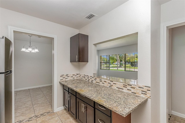 kitchen with stainless steel fridge, decorative backsplash, light tile patterned flooring, light stone counters, and dark brown cabinets