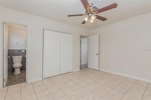 unfurnished bedroom featuring tile walls, a closet, light tile patterned floors, ornamental molding, and ceiling fan