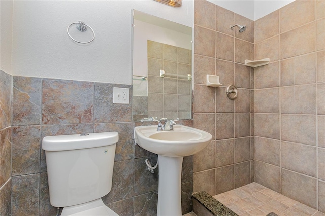 bathroom featuring tile walls, tiled shower, sink, and toilet