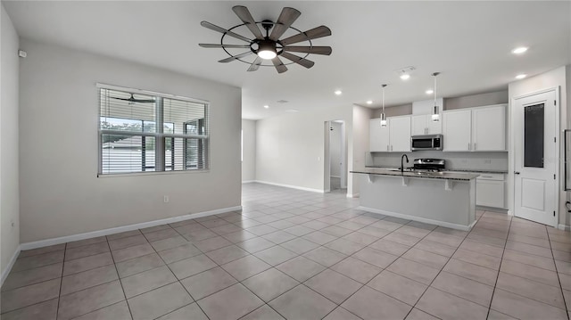 kitchen with an island with sink, ceiling fan, stainless steel appliances, hanging light fixtures, and white cabinetry