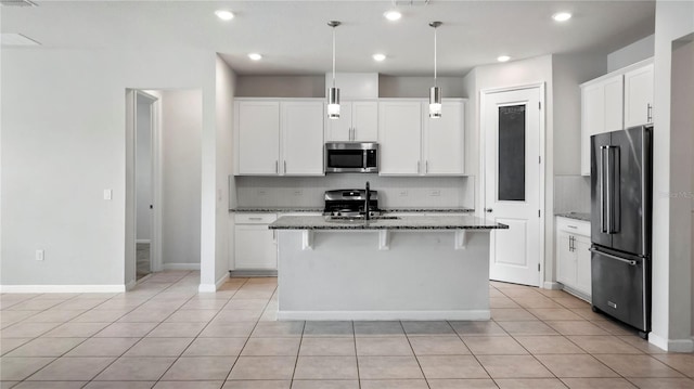 kitchen featuring a kitchen island with sink, stainless steel appliances, pendant lighting, white cabinetry, and stone counters