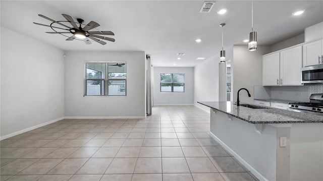 kitchen with stainless steel appliances, white cabinets, sink, dark stone counters, and hanging light fixtures