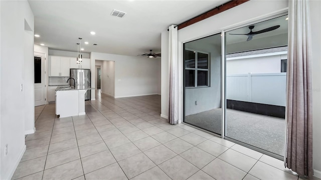 kitchen featuring an island with sink, a breakfast bar, white cabinets, stainless steel refrigerator, and decorative light fixtures