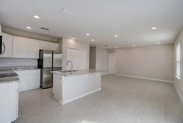 kitchen with appliances with stainless steel finishes, white cabinets, light stone countertops, a center island with sink, and sink