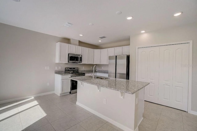 kitchen with white cabinetry, light stone counters, stainless steel appliances, a kitchen island with sink, and sink