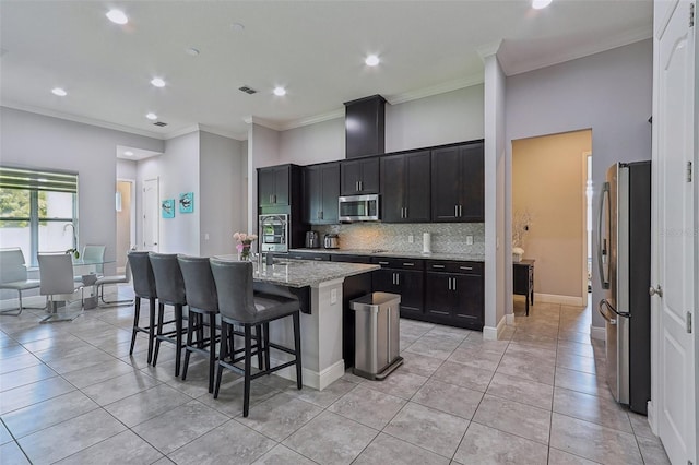 kitchen featuring a breakfast bar, light stone counters, stainless steel appliances, a center island with sink, and crown molding