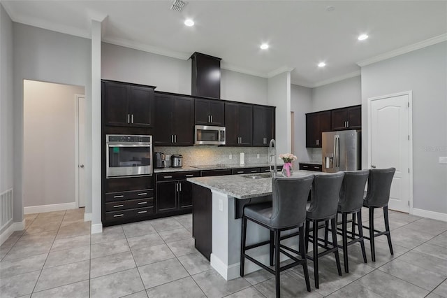 kitchen featuring sink, a center island with sink, appliances with stainless steel finishes, a kitchen breakfast bar, and crown molding