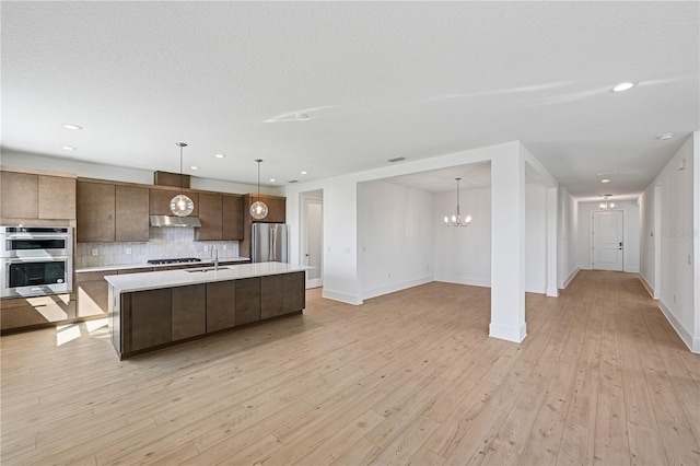 kitchen with backsplash, light countertops, light wood-style flooring, stainless steel appliances, and a sink