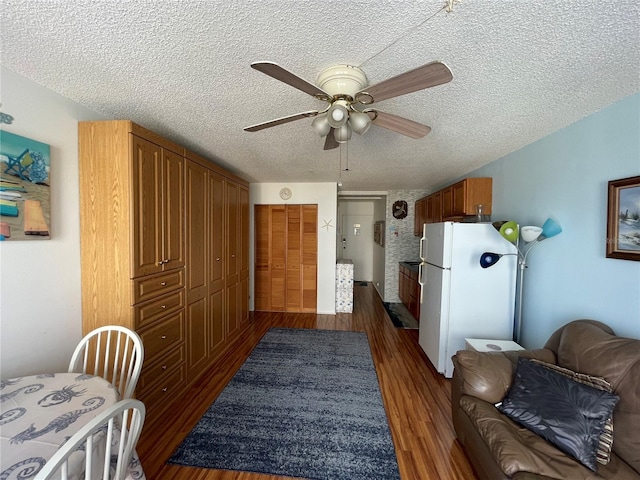 interior space with a textured ceiling, dark wood-type flooring, ceiling fan, and white refrigerator