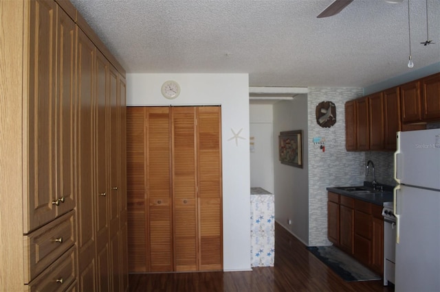 kitchen with white appliances, a textured ceiling, sink, ceiling fan, and dark wood-type flooring