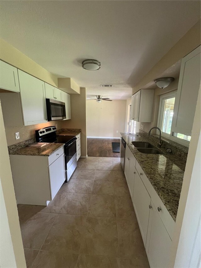 kitchen with dark stone counters, sink, white cabinetry, appliances with stainless steel finishes, and light tile patterned floors