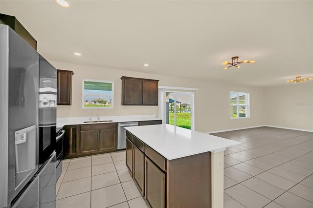 kitchen with light tile patterned floors, sink, dark brown cabinets, stainless steel appliances, and a center island