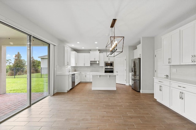 kitchen with white cabinets, stainless steel appliances, decorative light fixtures, and a healthy amount of sunlight