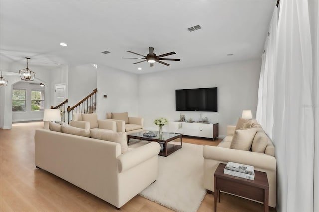 living room with ceiling fan with notable chandelier and light hardwood / wood-style flooring