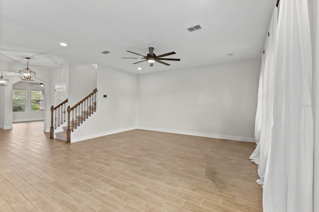 empty room featuring ceiling fan with notable chandelier and light hardwood / wood-style flooring