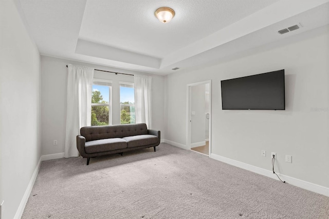 living area with a textured ceiling, a tray ceiling, and light carpet