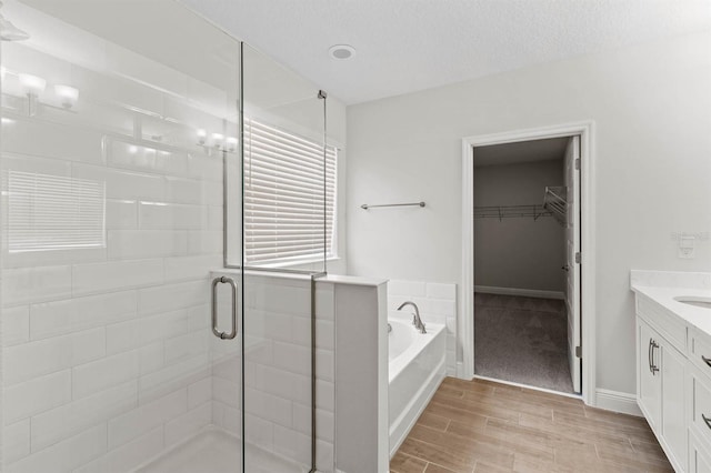 bathroom with a textured ceiling, independent shower and bath, hardwood / wood-style flooring, and vanity