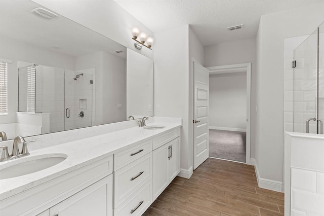 bathroom with wood-type flooring, vanity, a shower with shower door, and a textured ceiling