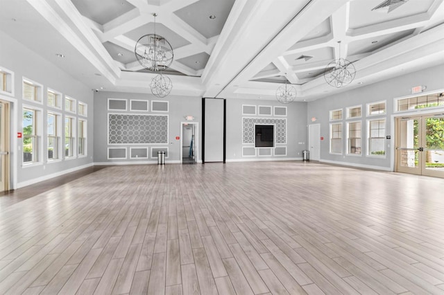 unfurnished living room featuring a notable chandelier, beam ceiling, light hardwood / wood-style floors, and coffered ceiling