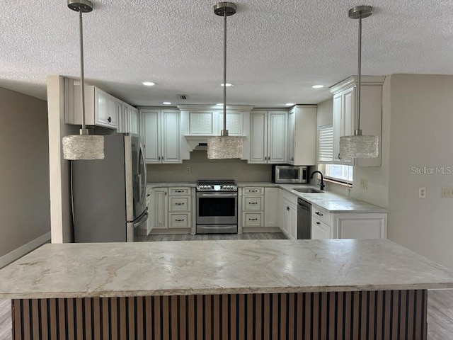 kitchen featuring a textured ceiling, light wood-type flooring, sink, pendant lighting, and stainless steel appliances