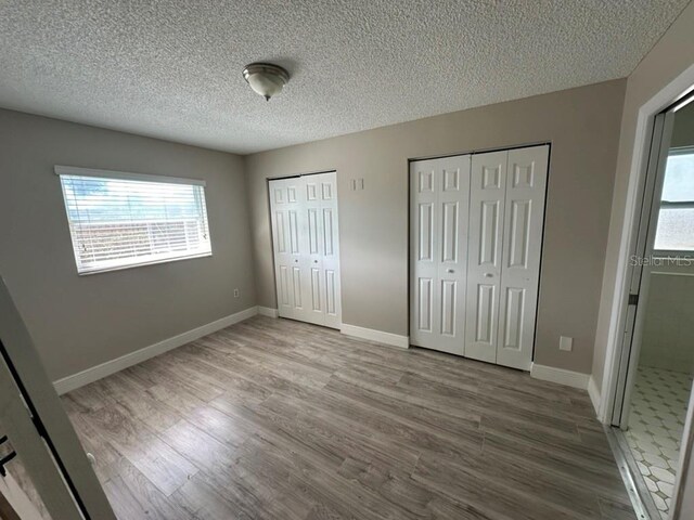 unfurnished bedroom featuring hardwood / wood-style floors, two closets, and a textured ceiling