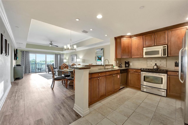 kitchen with ceiling fan, kitchen peninsula, stone counters, appliances with stainless steel finishes, and a tray ceiling