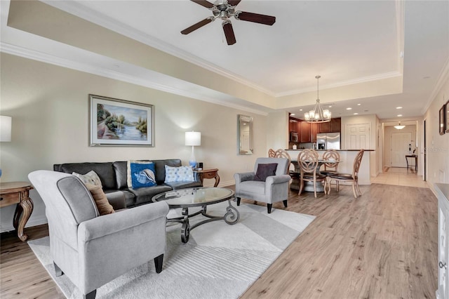 living room featuring ceiling fan with notable chandelier, crown molding, light hardwood / wood-style floors, and a tray ceiling