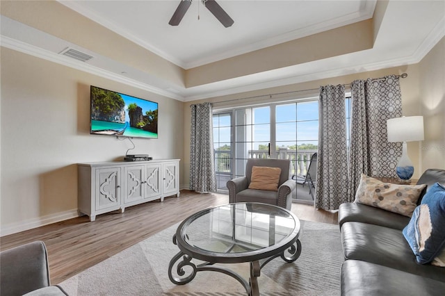 living room featuring light wood-type flooring, a raised ceiling, ornamental molding, and ceiling fan