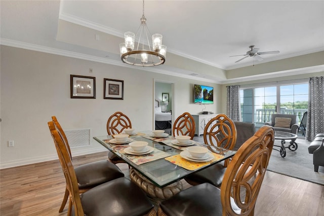 dining room with ceiling fan with notable chandelier, light hardwood / wood-style flooring, crown molding, and a tray ceiling