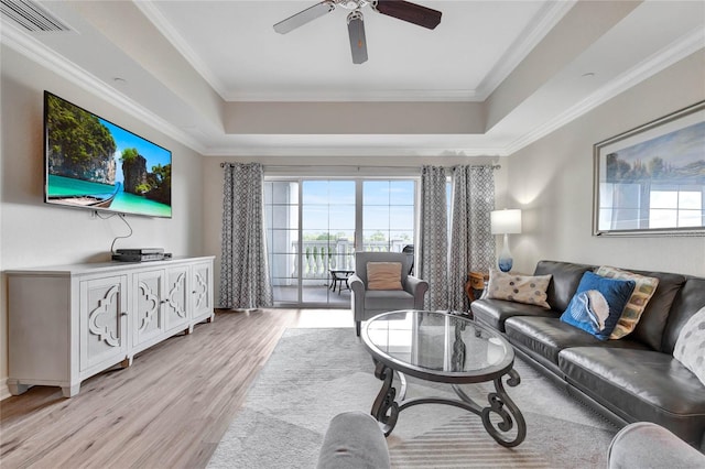 living room with ornamental molding, light wood-type flooring, ceiling fan, and a raised ceiling