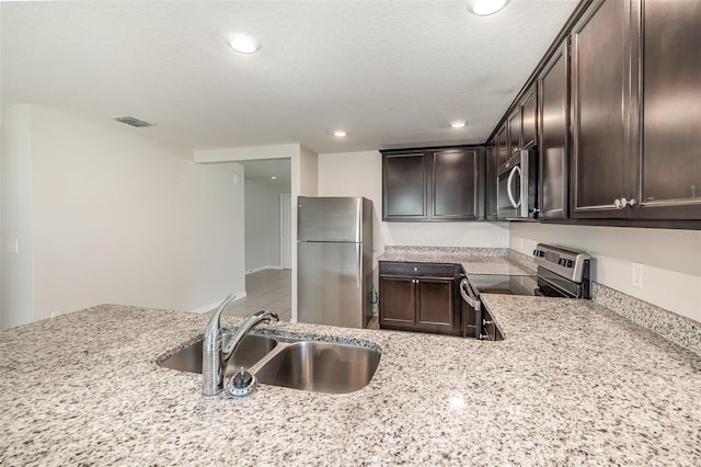 kitchen featuring appliances with stainless steel finishes, light stone counters, a textured ceiling, dark brown cabinetry, and sink