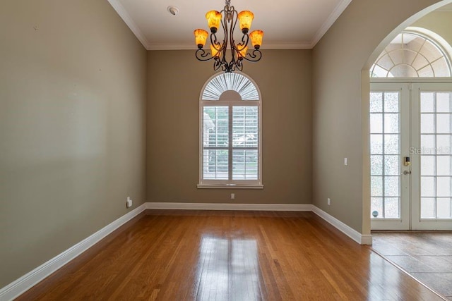 empty room with wood-type flooring, ornamental molding, a notable chandelier, and french doors