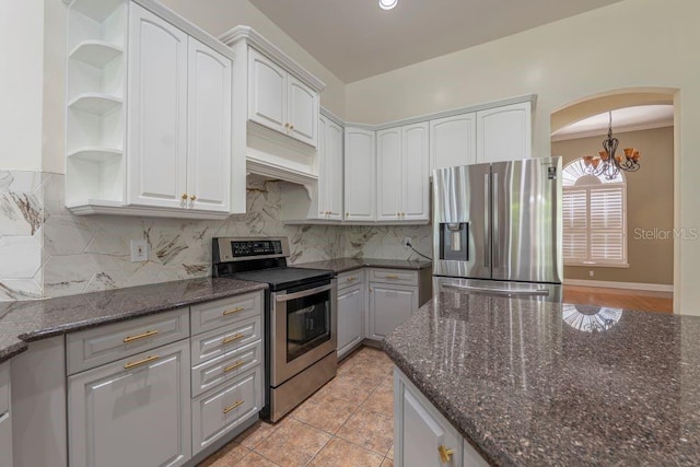 kitchen featuring white cabinets, light tile patterned floors, stainless steel appliances, a notable chandelier, and dark stone counters